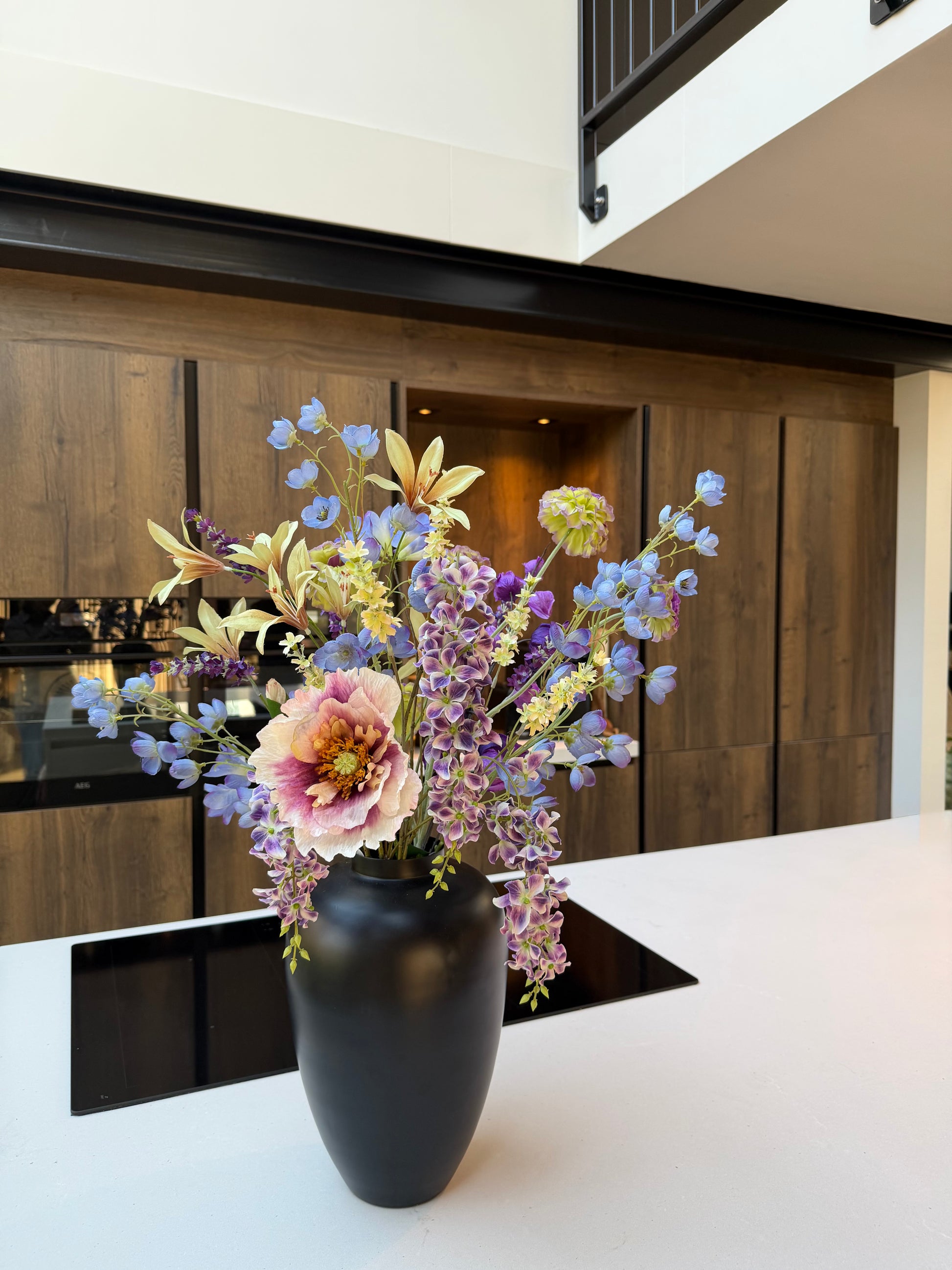 Groot zijden veldboeket met roze klaproos en blauw, groene en paarse bloemen in zwarte vaas. - Bloomley